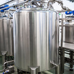 <Several large, cylindrical, shiny stainless steel mixing tanks and pipework in a dietary supplement manufacturing unit with gantry, grey non slip floor and white ceiling. Credit> AdobeStock_383238064